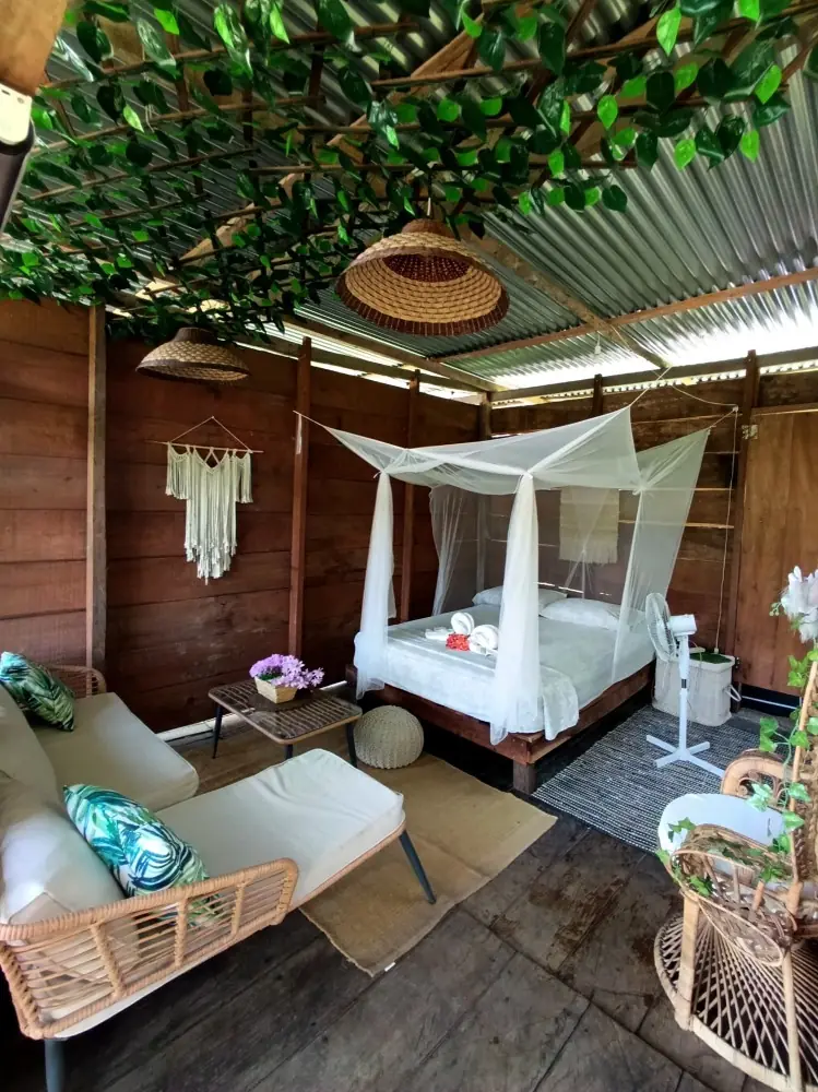 Cama con dosel de mosquitero bajo techo de zinc, con pared de follaje verde