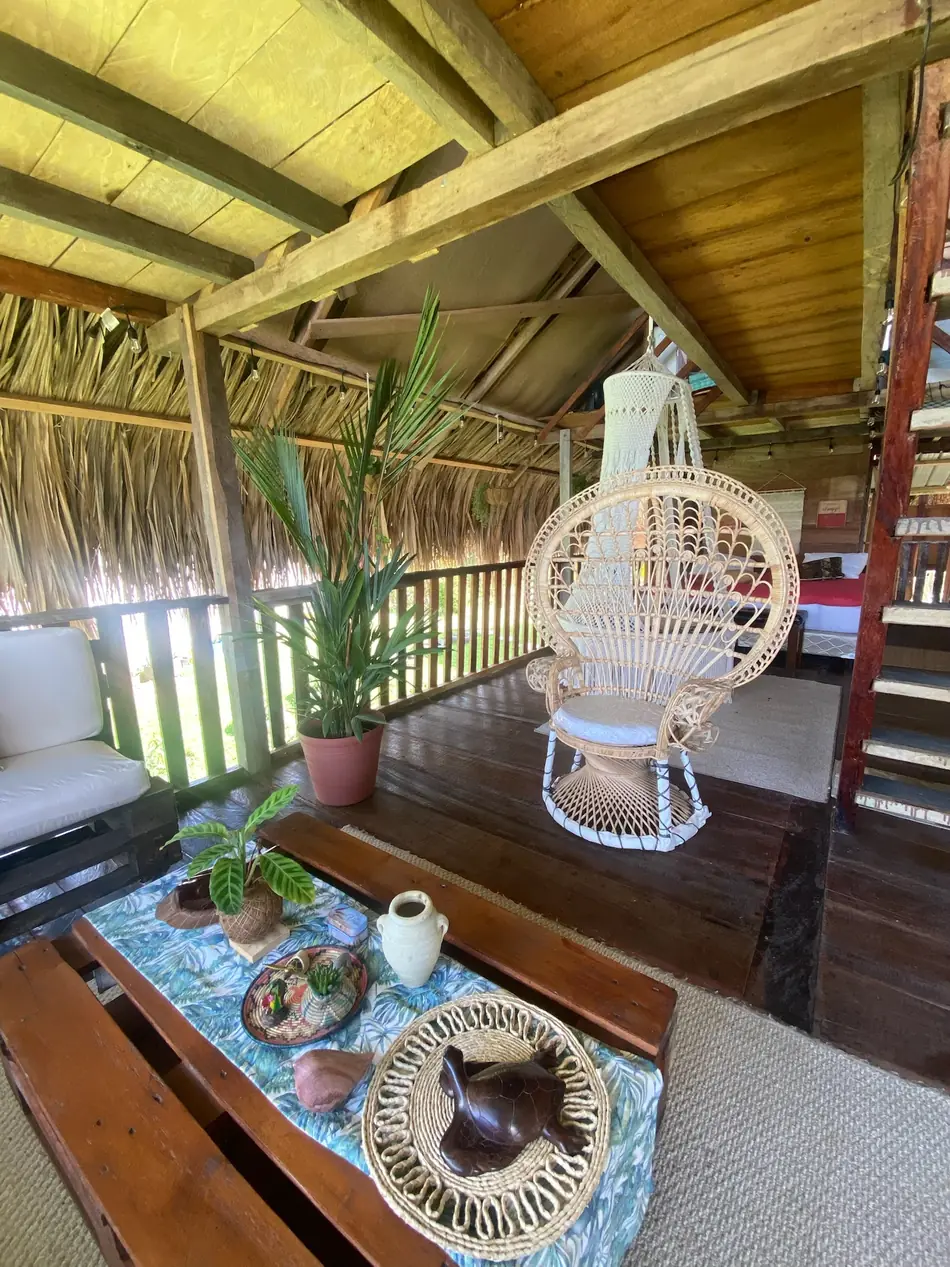 Silla colgante de ratán junto a la cama, con el deck de madera al fondo