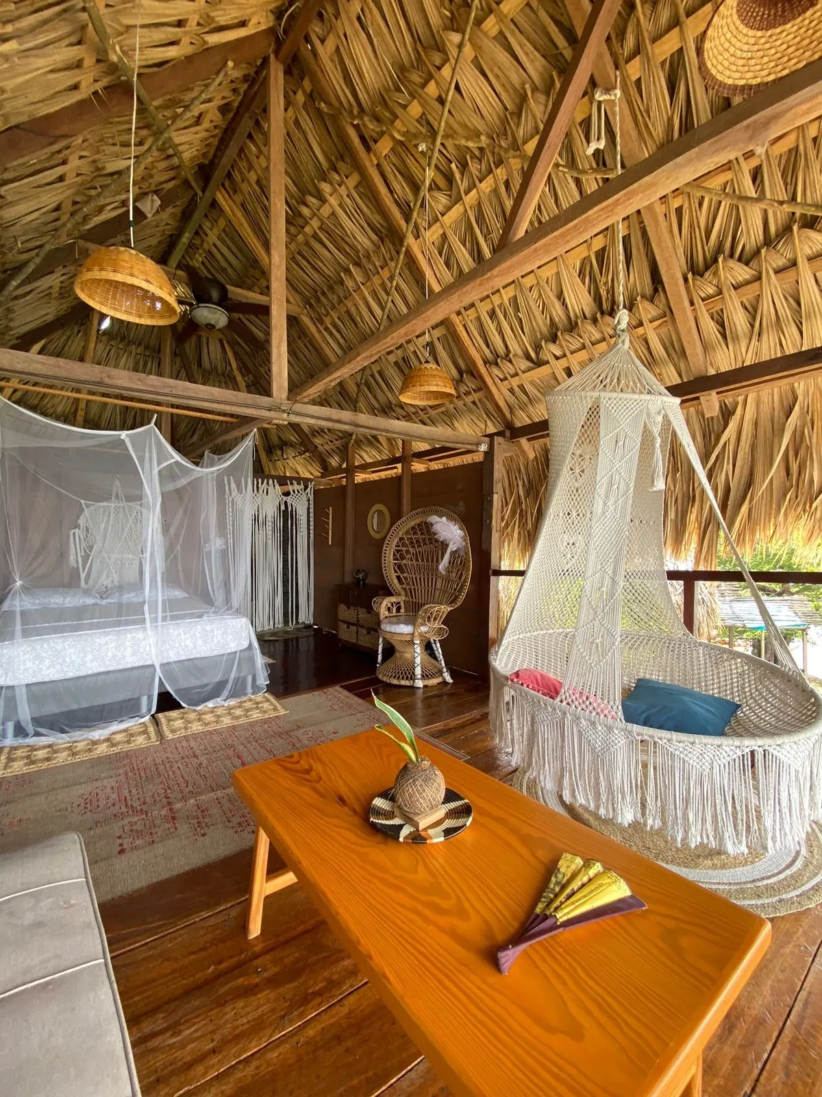 La sala junto a la cama, con silla de mimbre en forma de pavo real y la silla colgante de macramé al fondo.