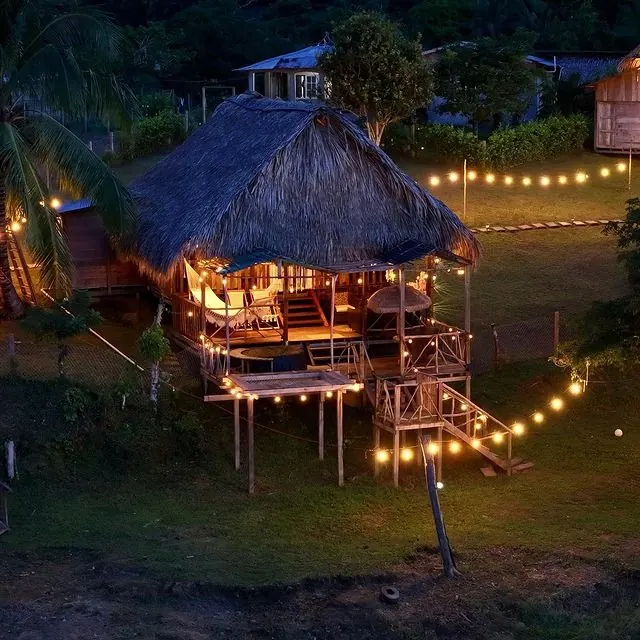 La cabaña de noche, iluminada con luces cálidas hasta el sendero del jardín.