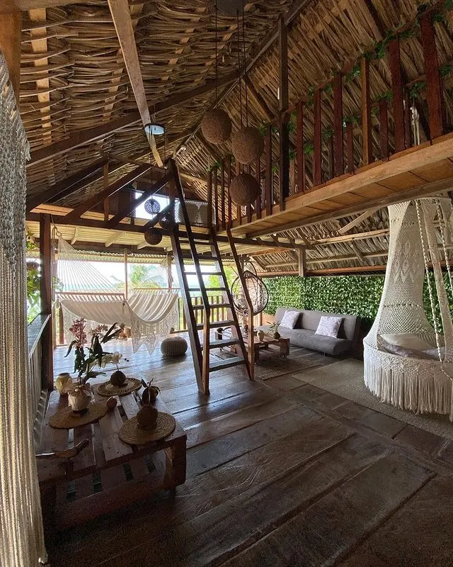 La sala de dos pisos, con escalera de mano al altillo, silla colgante de macramé y sofá.