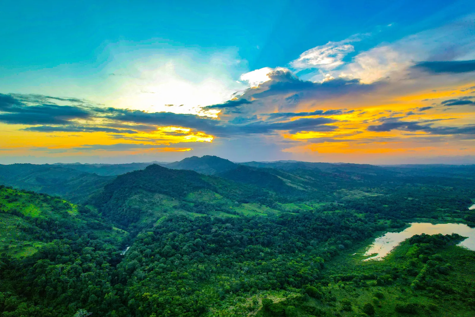 Vista aérea del valle de Bayano al atardecer, con el lago al fondo entre colinas de selva